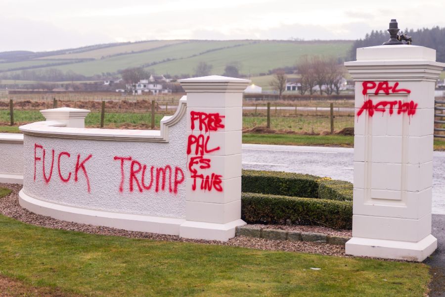 Graffiti on a white stone wall reads "F*** Trump" and "Free Palestine," alongside messages advocating for Palestinian action.