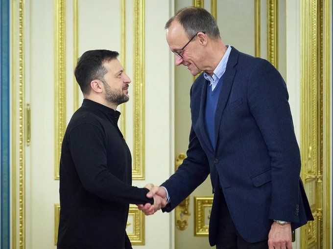 Zelenskyy and Mertz shake hands in an ornate indoor setting, marked by golden details and an elegant atmosphere. 