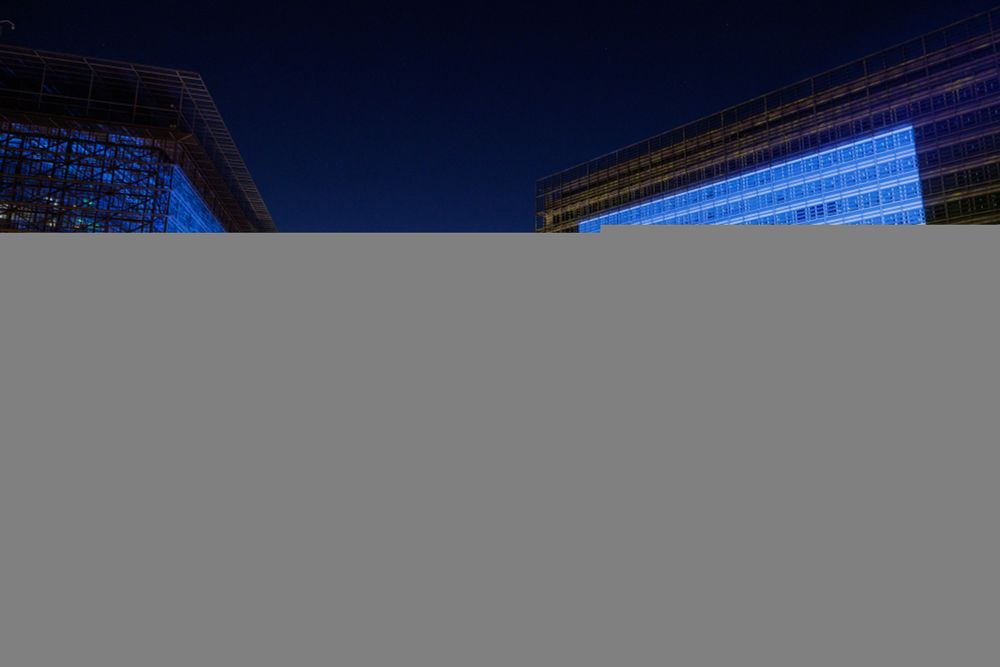 Buildings illuminated in blue and yellow, representing the Ukrainian flag, against a twilight skyline with a lit street below.