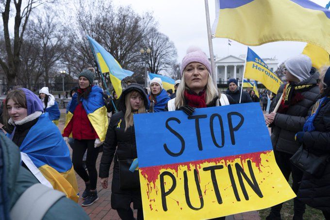Protesters hold Ukrainian flags and a large sign reading "STOP PUTIN" during a rally advocating for peace and support for Ukraine.