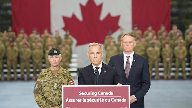 Carney on podium that reads securing Canada, massive Canadian flag in background and troops.