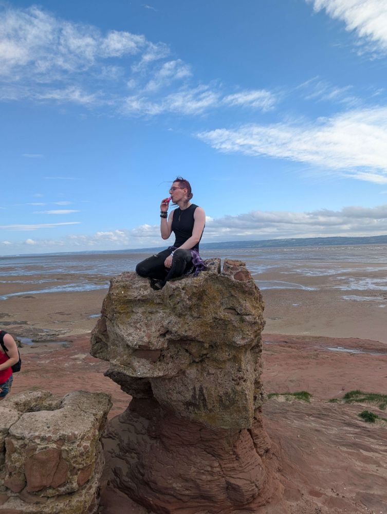 Luci sat cross legged on a cool rock with the sea behind her, entirely in her own world and vaping.