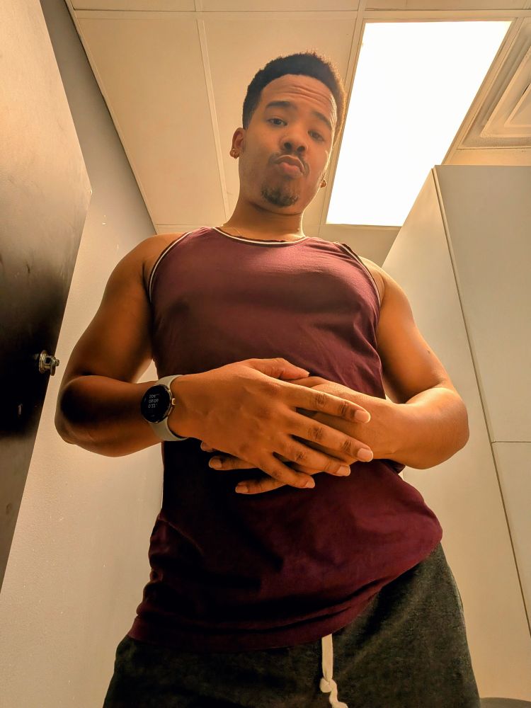 A picture of me in the locker room at the gym after a push workout, I'm wearing a maroon tank top and gray shorts and leaning slightly away from the camera while poking my lips out, for some reason. 