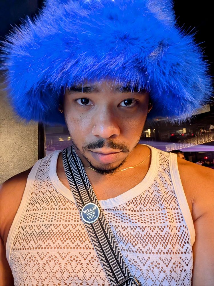 A close-up picture of me in a fuzzy, bright blue bucket hat with a white lacey tank top on. I am staring deep into your eyes with a pleading look to convince you to come up off that phone.