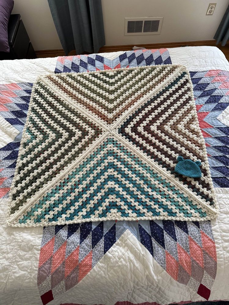 Picture of a baby blanket I crocheted. It's a square of 4 triangle motifs made of granny stripes. The stripes alternate white with a brown/tan/green/blue ombre.