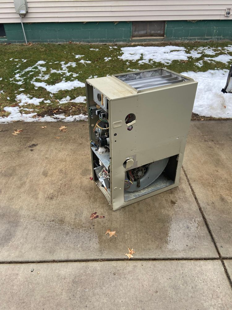 Old beige rectangle that is a furnace on a concrete driveway outside sadly in snowy conditions 