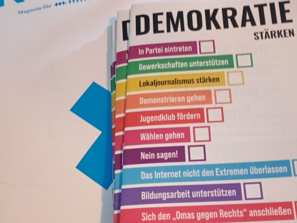 Ein Stapel Flyer, darauf die Aufschrift: Demokratie stärken.
Dann, mit jeweils unterschiedlichen Farben hinterlegt, die Checkpoints:
In Partei eintreten 
Gewerkschaften unterstützen 
Lokaljournalismus stärken
Demonstrieren gehen
Jugendklub fördern
Wählen gehen
Nein sagen!
Das Internet nicht den Extremen überlassen
Bildungsarbeit unterstützen 
Sich den "Omas gegen Rechts" anschließen