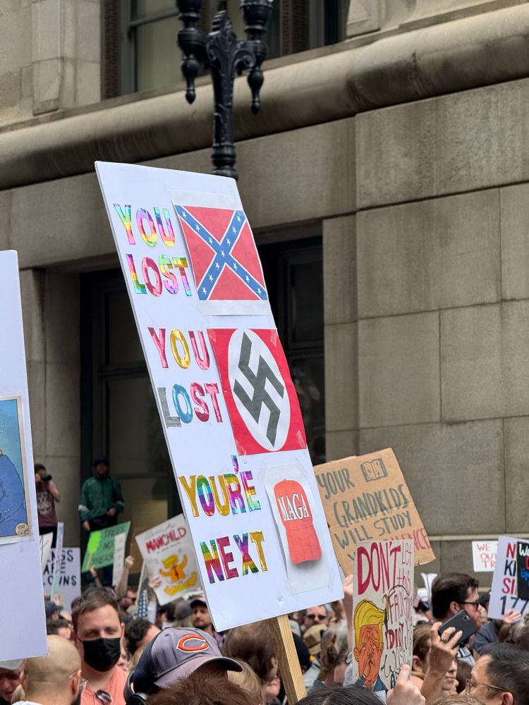A sign at a protest reads “you lost” next to a Confederate flag, “you lost” next to a Nazi flag, and “you’re next” next to a MAGA hat. 