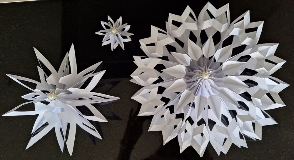 Schneesterne aus festem Papier. Entworfen, skizziert,  geklebt, geschnitten, nochmals geklebt und mit Perlen in der Mitte verziert.