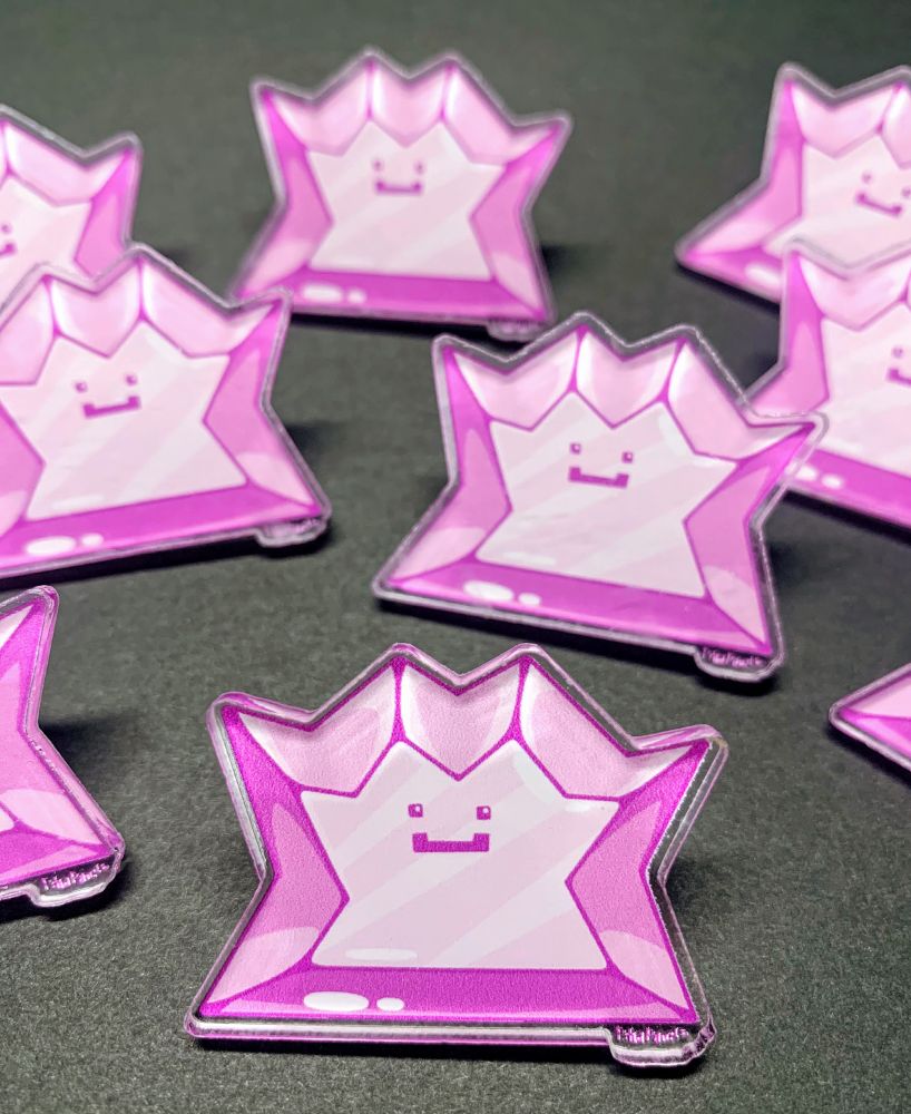 Acrylic pins of the pink Pokemon Ditto designed to look like a gemstone with angular sides and shiny highlights.