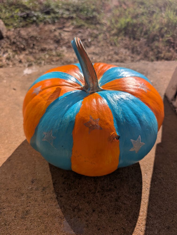 A pumpkin painted with orange and teal stripes with silver stars drawn on it