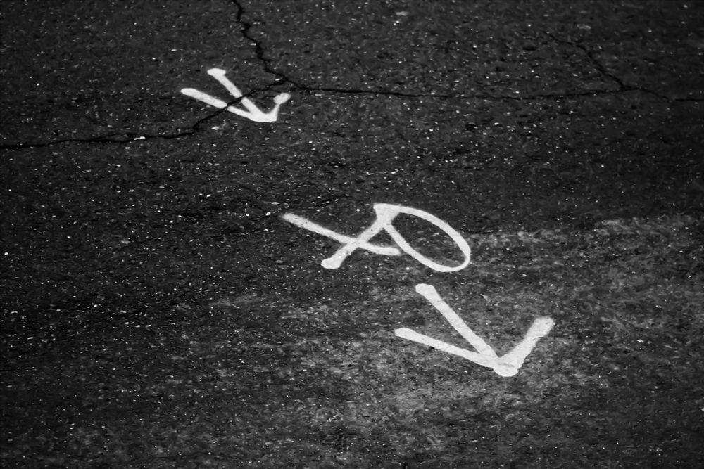 A road with white spray paint of two arrows around an X and an O.