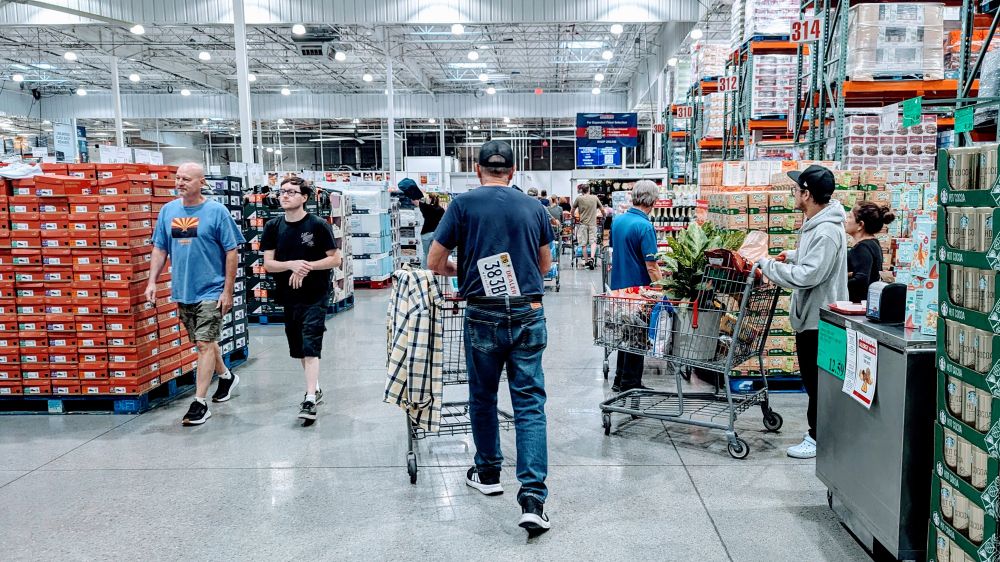 Photograph of shoppers in the Isle of a Costco, pushing shopping carts and gathering various things. 

In the center of the frame there is a gentleman pushing a shopping cart walking away from the camera and visible sticking out of the back of his jeans, tucked in by his butt, is clearly a vehicle license plate. 

Why this is the case is not explained.  Or possibly even explainable.