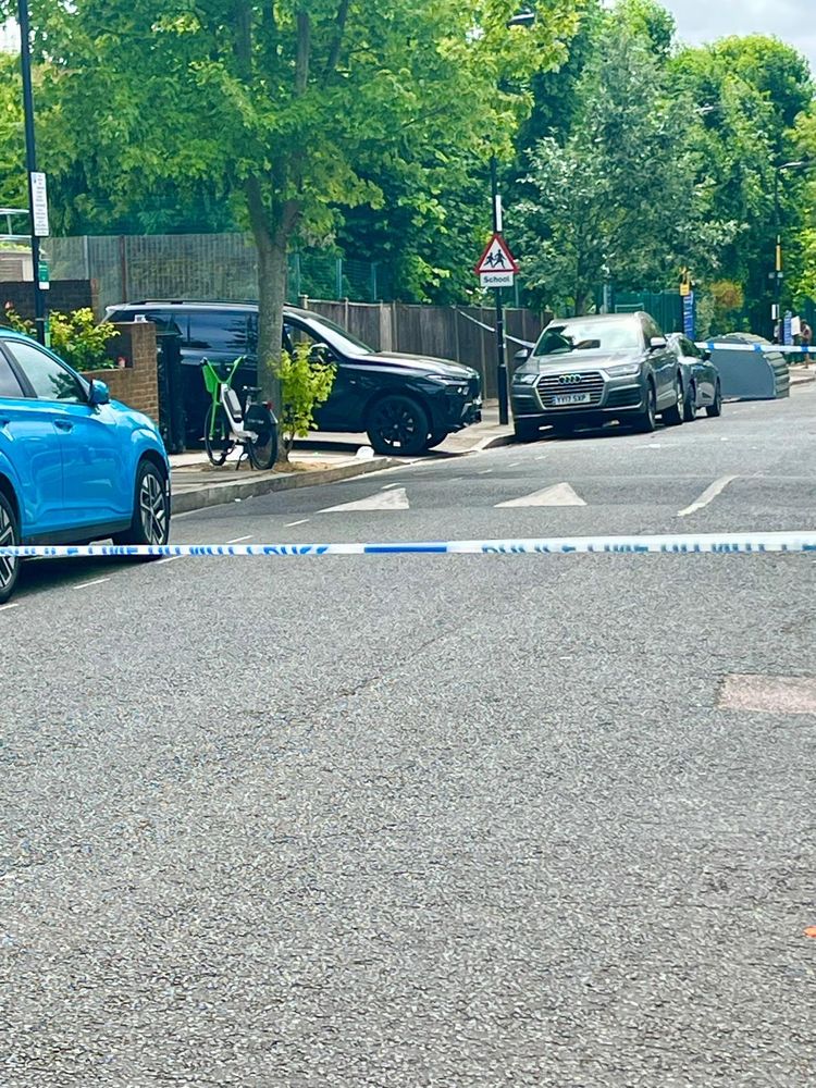 A picture of a SUV car on a pavement outside a school. A bike is in front of the bike