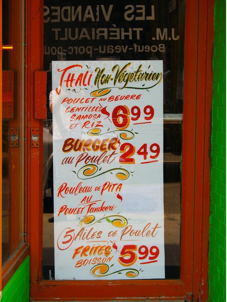 A doorway with a sandwich board promoting thali, burgers, pita sandwiches, and chicken wings in French.