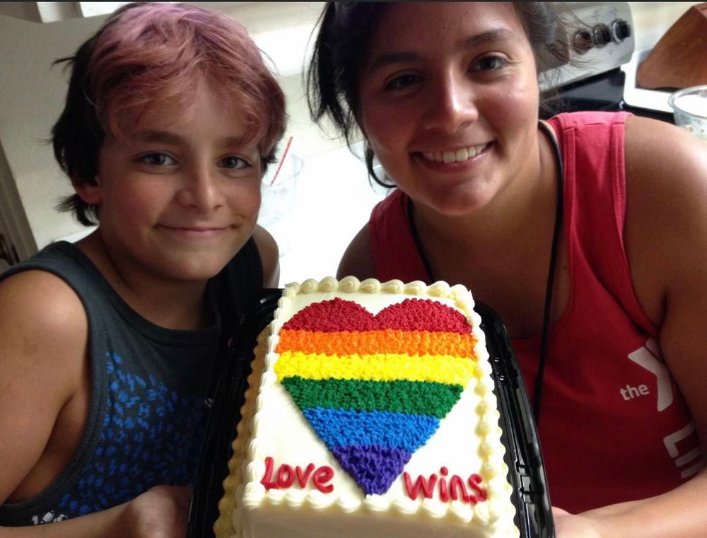A 10-year-old boy and his 19-year-old sister holding up a cake decorated with a rainbow heart that reads, “love wins.”
