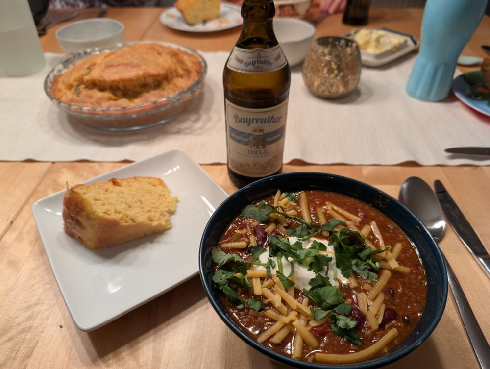 Homemade chili with cheese, sour cream, and cilantro. Accompanied with homemade corn bread and a beer (not homemade)