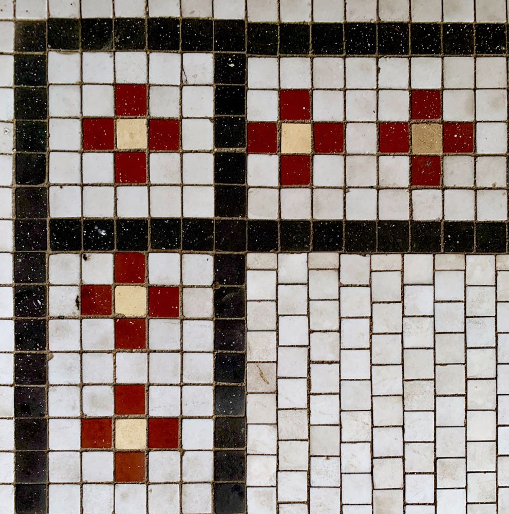 The corner detail of a vintage tile floor circa 1920s with white, red, yellow and black square tiles.