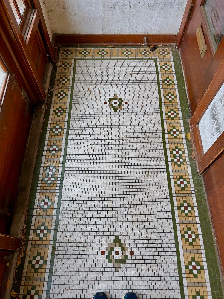 A narrow vestibule in a vintage apartment building, circa 1910 has plenty of doorways and tile floor that has lasted through the decades, showing some cracking that does don’t diminish its usefulness. 