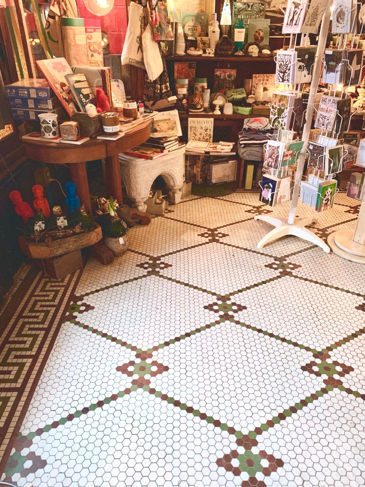 A local store filled with gift items and cards atop a red, green and white vintage tile floor circa 1900. 