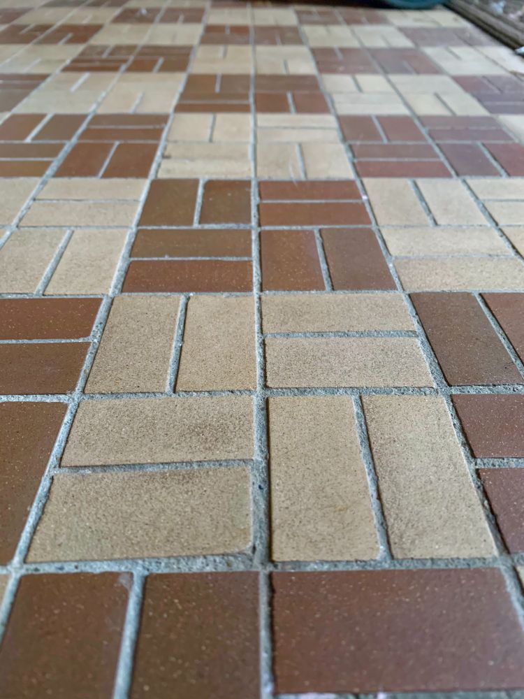 A close up of a brown and tan checked vintage tile floor taken at approx 30 degree angle. 