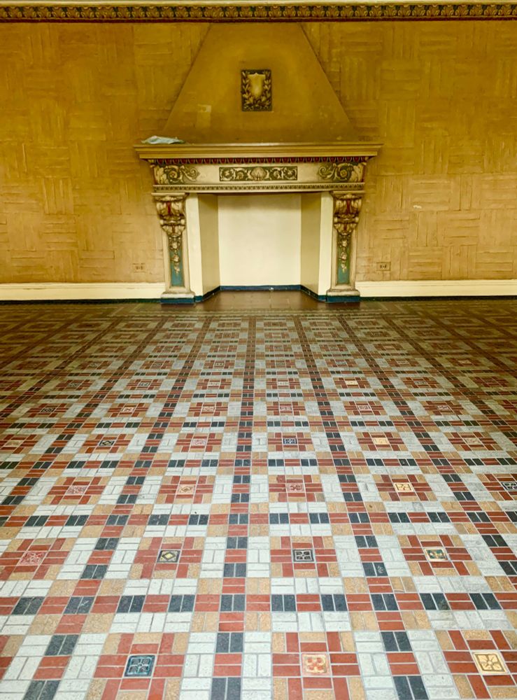 A decorative fireplace, faux basketweave wall treatment and a colorful vintage tile floor are unique features of this vintage apartment building's warm entrance hallway.