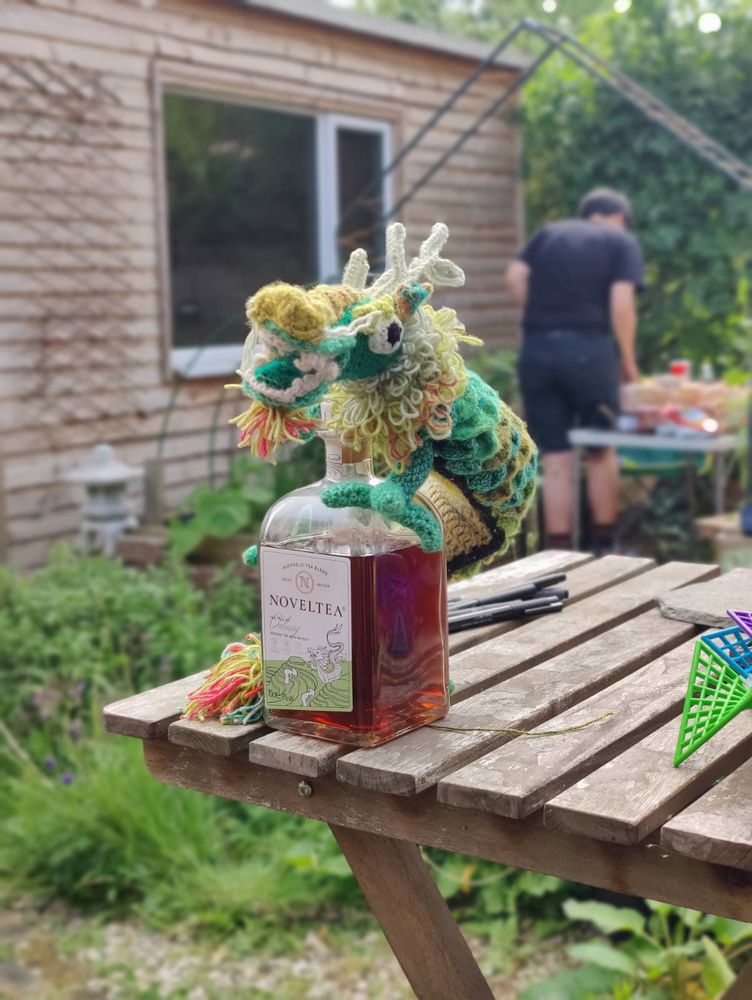 An Asian-style long dragon with four feet, crocheted from different shades of green, yellow, and orange yarn. It has big bulgy eyes, lots of teeth, whiskers, and coral-like horns. And a pompom tail.