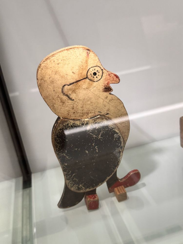 A large wooden toy - body shaped like a black bird, wearing brown boots, head shaped like a bald man with glasses, moustache and a reddish nose