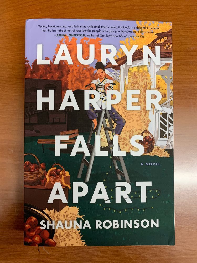 book cover for lauryn harper falls apart by shauna robinson with white block lettering over an illustration of a brown skinned woman astride a ladder wrapped in string lights and surrounded by an autumn village green scene