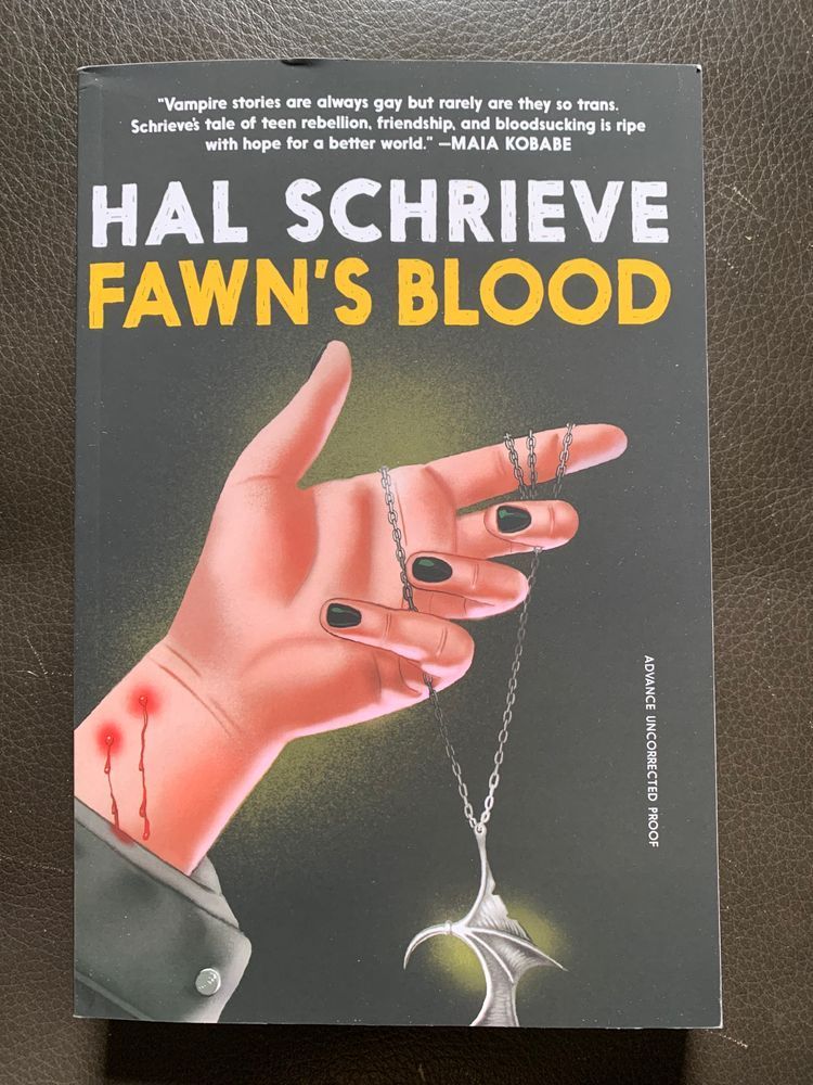 book cover for fawn's blood by hal schrieve with white and yellow lettering over a dark background with an image of a hand with black painted nails holding a silver necklace. on the wrist of the hand are two puncture wounds dripping blood