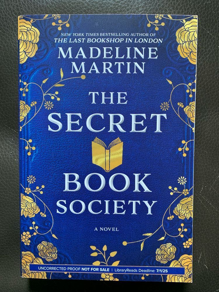 book cover for the secret book society by madeline martin with white lettering over a deep blue background designed to look like a gilded and tooled leather book cover with gold floral embellishment