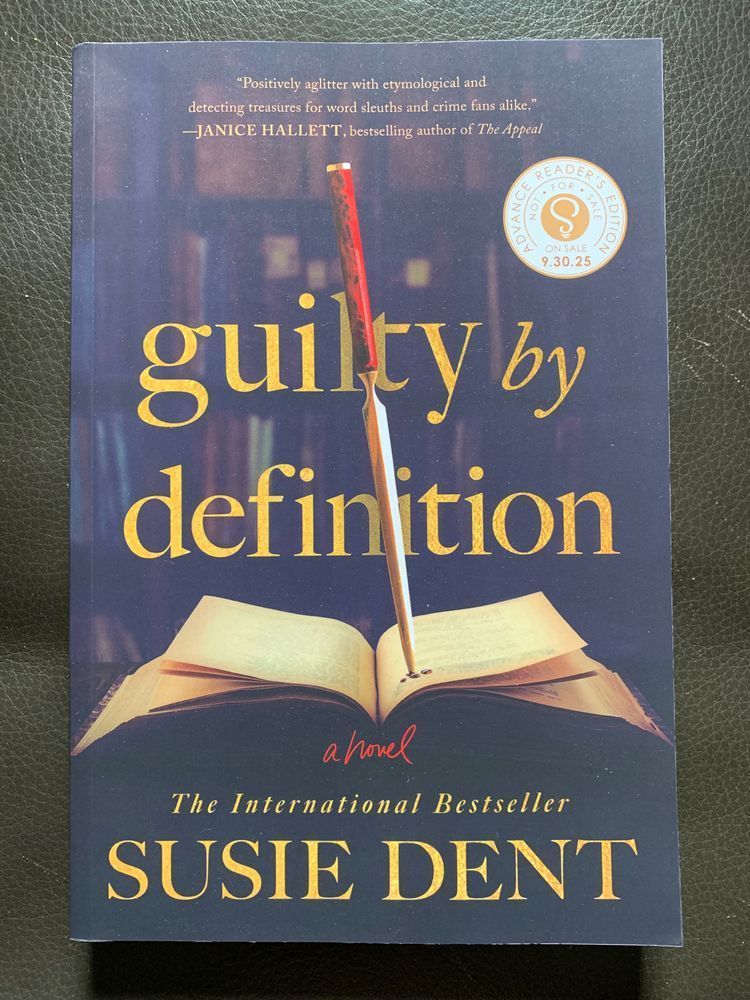 book cover for guilty by definition by susie dent with yellow lettering over a dark background picturing a crowded bookshelf. in the foreground is an open book with a stiletto stabbing into the right hand pages