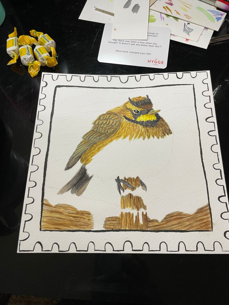 A photo of a partially finished watercolor painting of a horned lark in an ink outline of a postal stamp 