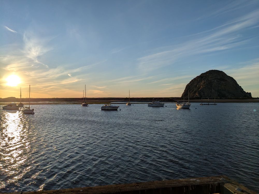 A coastal bay at sunset. Several small sailboats are attached to a dock.