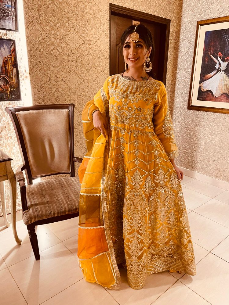 Woman standing next to a chair while wearing yellow and gold Pakistani wedding attire