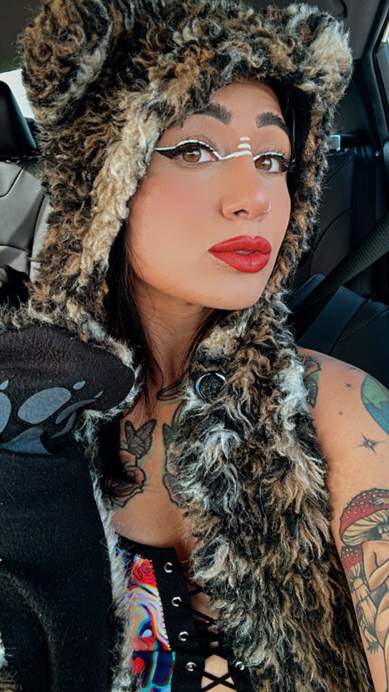 Selfie of a woman wearing a leaopord beanie hood, and an Alice in wonderland crop top.