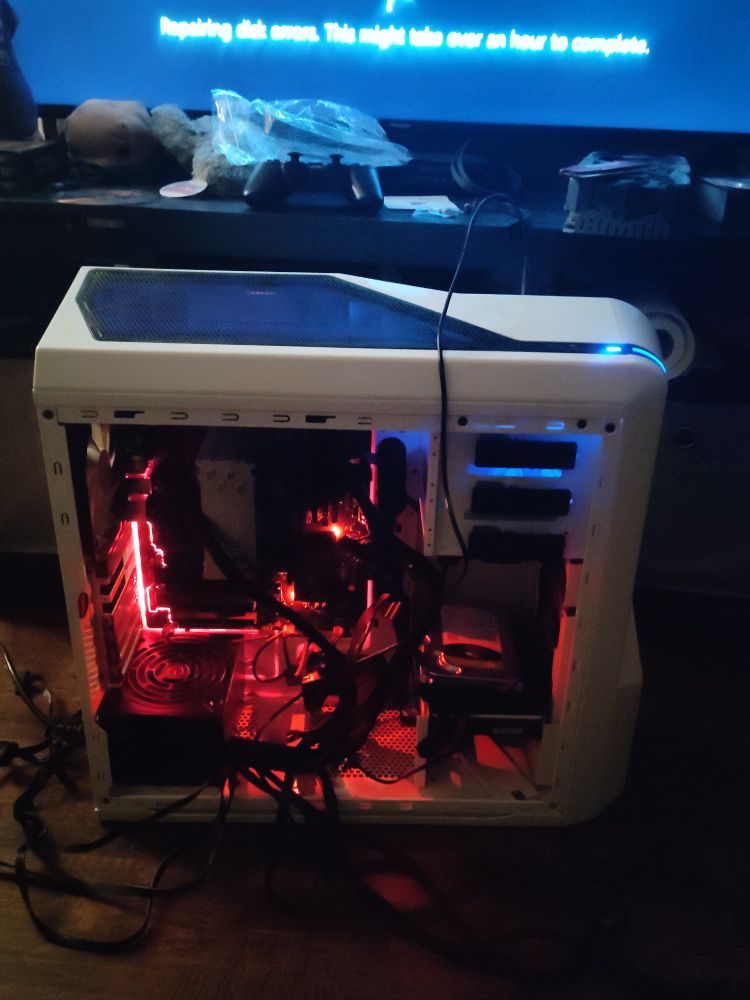 Computer with the side panel off and several cables spilling out. On the screen it says "repairing disk errors. This might take over an hour to complete"