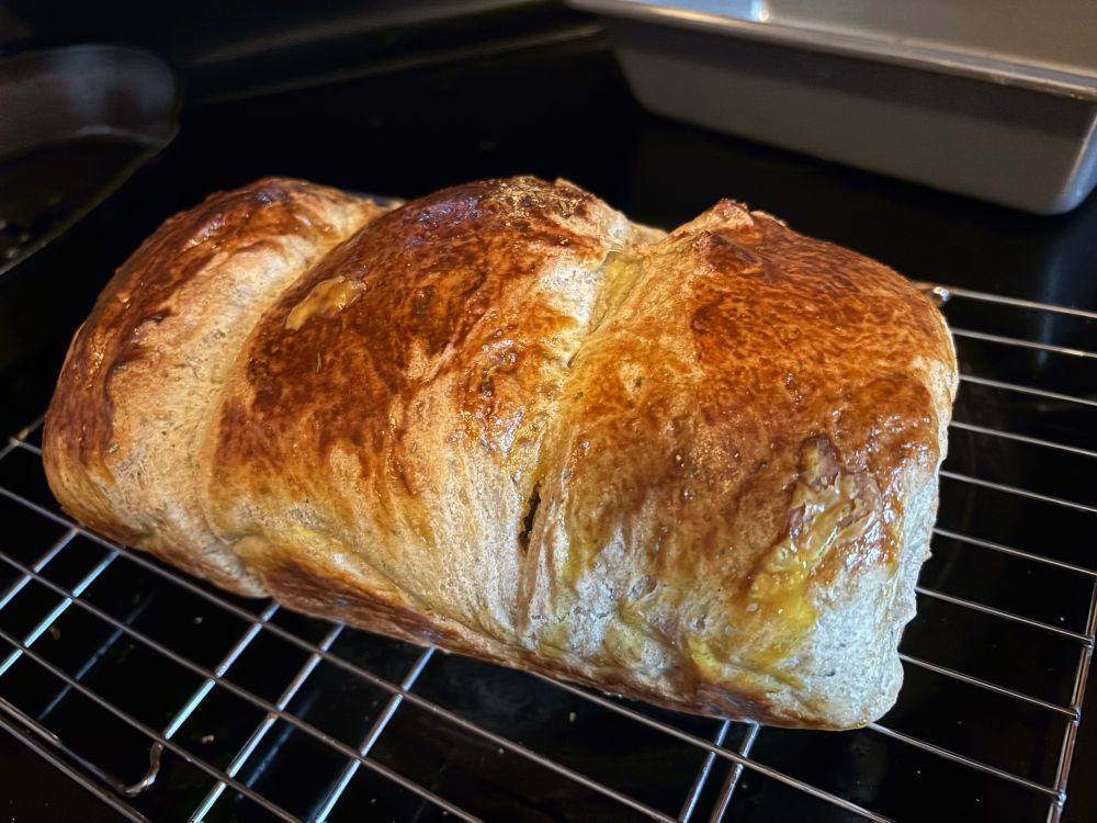 A fresh loaf of homemade bread sitting on a wire cooling rack.