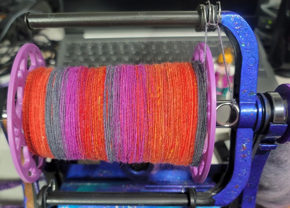 Spinning singles of a Good Karma Farm batt in grey, magenta, and orange on an Electric Eel Wheel 6.0.