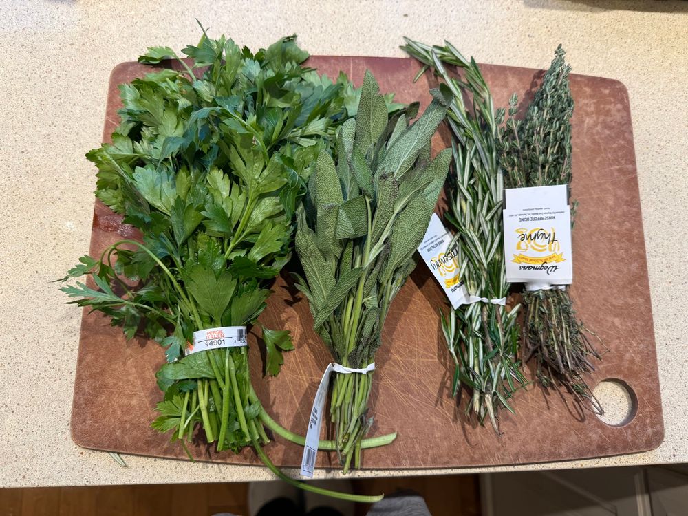 A cutting board with bunches of fresh parsley, sage, rosemary, and thyme 