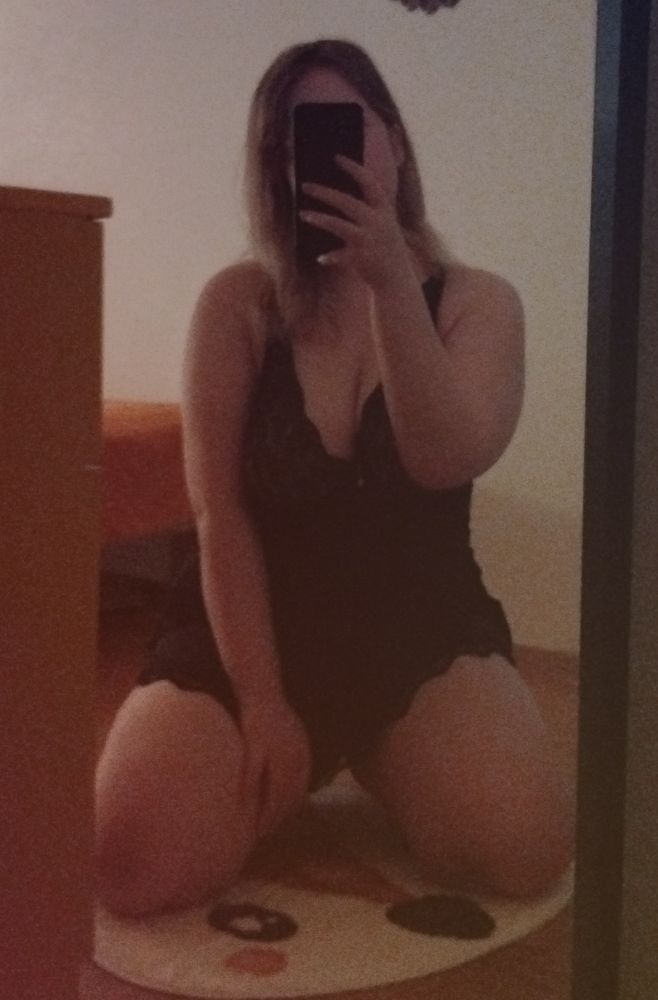 mirror selfie of emma wearing a black babydoll nightgown, sitting on her wide spread knees, one hand on her inner thigh