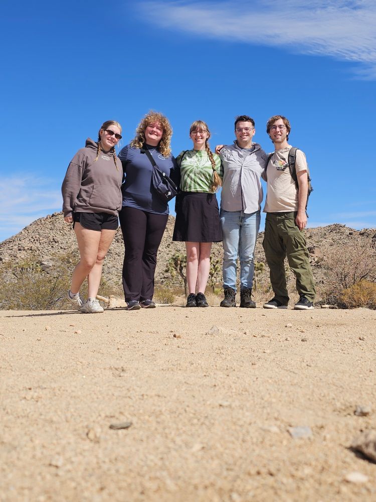 A group of 5 people standing shoulder to shoulder smiling at a camera on Joshue Tree National Park.
