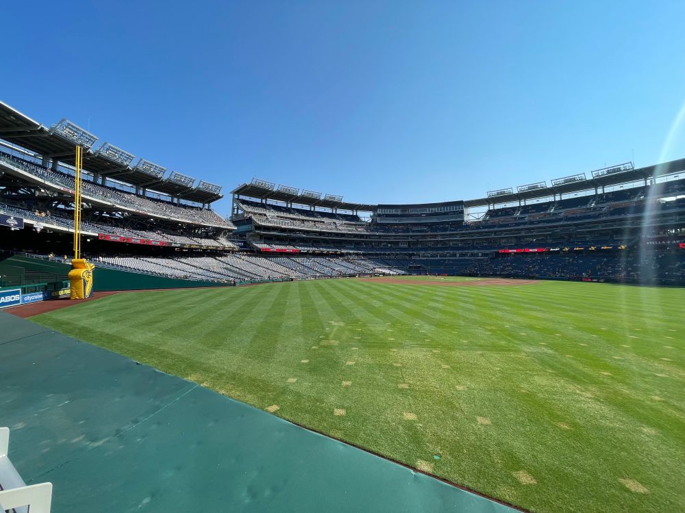 A wide angle photograph of a still-filling-up Nationals Park, a baseball field in Washington DC. Graphics on the scoreboards reflect a Banana Ball game between the Bananas and the Firefighters.