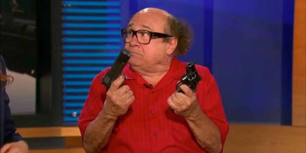 IASIP character Frank Reynolds (Danny Devito) wearing a red shirt and holding one gun in each hand while looking to his right