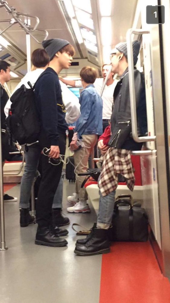 candid shot of Jimin and yoongi on an airport train, but it actually looks like it could be any old city subway. jimin looks like he's been caught mid-sentence and is wearing a grey beanie, long sleeved black shirt, black pants and black boots; his hair is brown and his bangs are fluffy over his forehead. he's wearing a backpack and in one hand he's holding a phone with the wired headphones still attached. across from him, Yoongi is leaning against the wall of the train car, and you can see from his side profile that he's smiling at Jimin. he looks very endeared and it is disgusting, please get a room!!!! anyways, he is also wearing a grey beanie, and is wearing glasses. he has a leather jacket draped over his shoulders and his hands are clasped in front of him; you can see that he's wearing a red long sleeved shirt. there's a white/red/black plaid flannel tied around his waist and he's wearing cuffed jeans and black doc marten boots. they look like they are having a subway meet-cute, like they're in their own little world and they can't even see the people around them. they are sickening!!!!!! can't stand them!!!!!!!!!!!!!!!!!!! I hope they get married