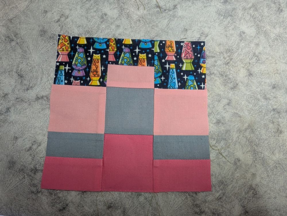 A block made of squares and rectangles. Three colors are solid; a light pink, medium grey, and dark pink while the last has kitty themed lava lamps in bright colors on a navy background
