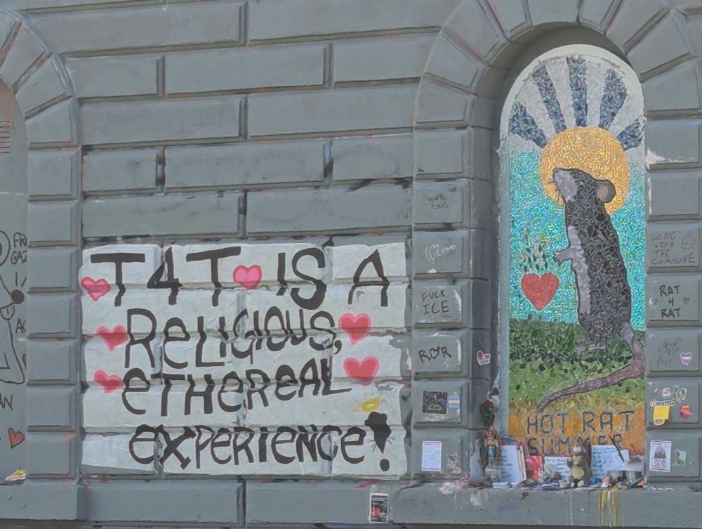 Photo of the Saint Rat hot rat summer mosaic. The mosaic depicted a rat with a golden halo and catholic burning heart. Next to it is graffiti reading T4T is a religious ethereal experience.