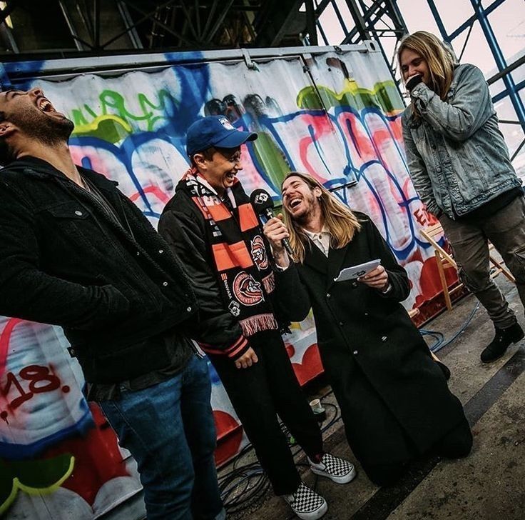 3 members of Nothing But Thieves, Conor Mason (middle), Dom Craik (left), and Joe Langridge-Brown (right) are being interviewed. The interviewer is kneeled beside Conor because he is short. Hilarity ensues.