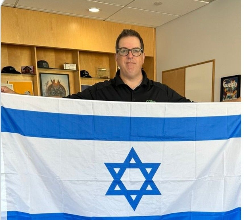 Photo of Guelph mayor Cam Guthrie holding up an Israeli flag for a photo op in the mayoral office.