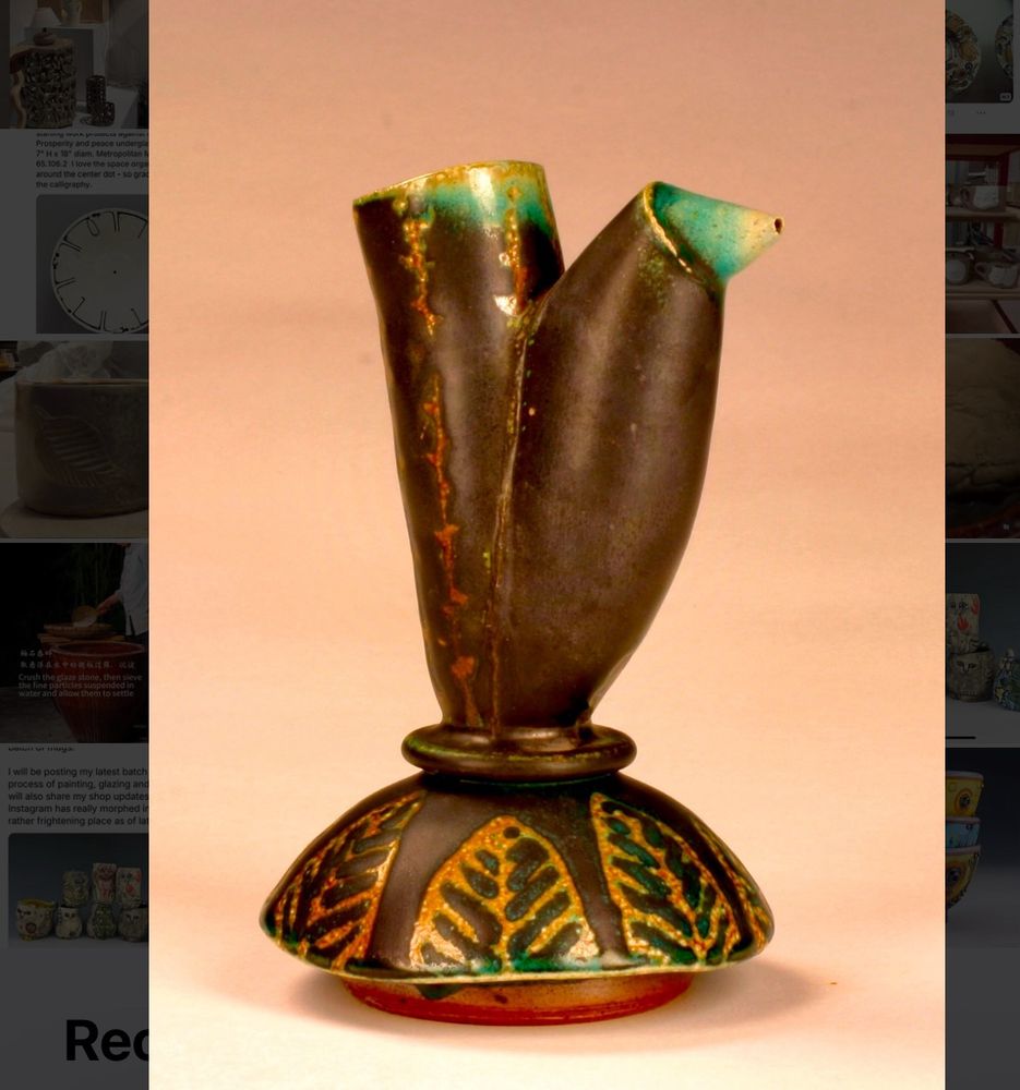 Soda fired pouring pot, blackish green with light green bleached tips from the firing process. Sitting in a holder with waxed out leaf patterns.